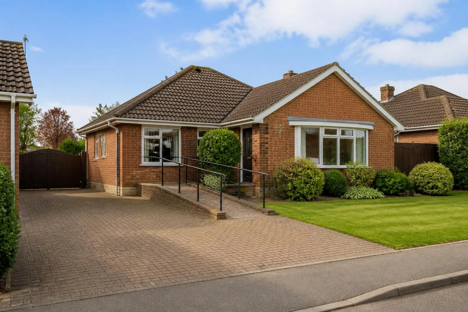 Representative red-brick supported-living bungalow in Northampton, with a ramped entrance, handrails, block-paved drive and front lawn