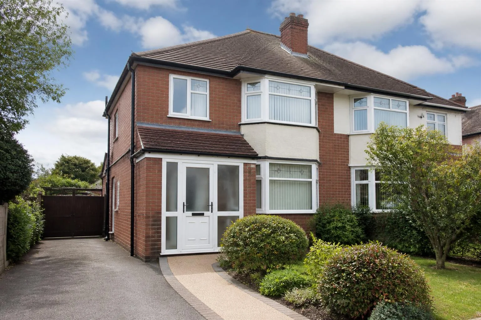 Representative red-brick supported-living home on a quiet Birmingham suburban street, with a level path and mature front garden
